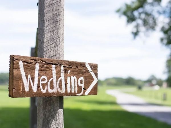 Rustic wooden sign pointing towards a wedding venue.
