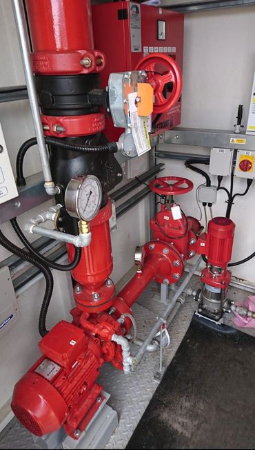 Red industrial pumps and valves in a mechanical room.
