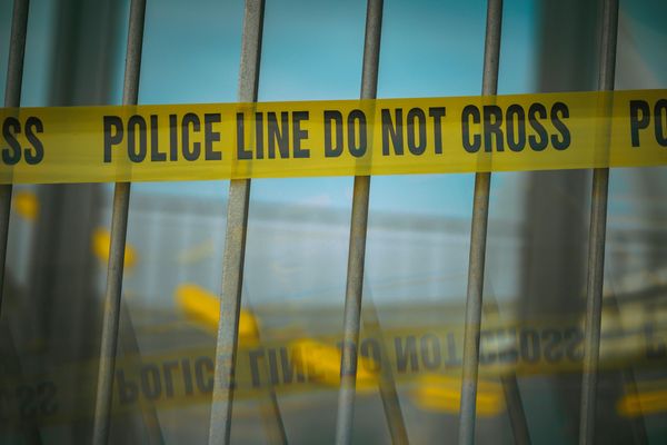 Yellow police tape reading 'POLICE LINE DO NOT CROSS' behind metal bars.
