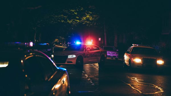 Police cars with flashing lights block a dark street at night.
