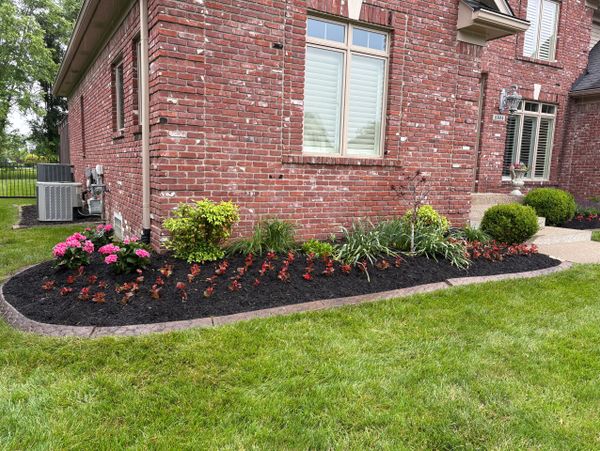 A neatly landscaped garden bed with colorful flowers along a brick house.