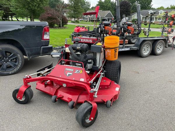 Red Ferris Z3X zero-turn mower parked near trailer with lawn equipment.