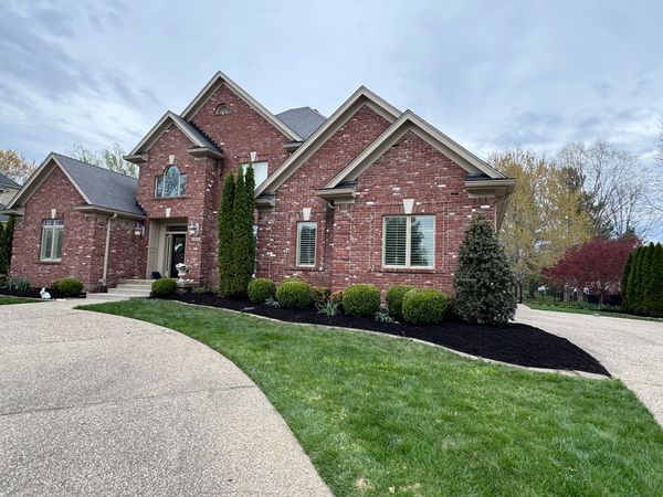 Large brick house with well-maintained lawn and shrubs under a cloudy sky.
