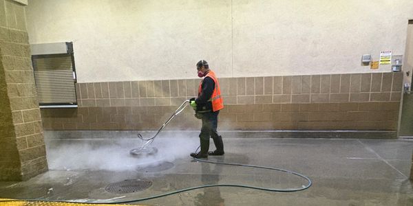 Worker power washing a concrete walkway at night.