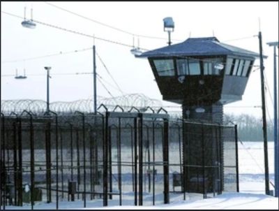 Prison watchtower and fences with barbed wire under a gray sky.