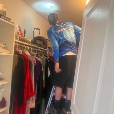 Person on ladder organizing clothes in closet.
