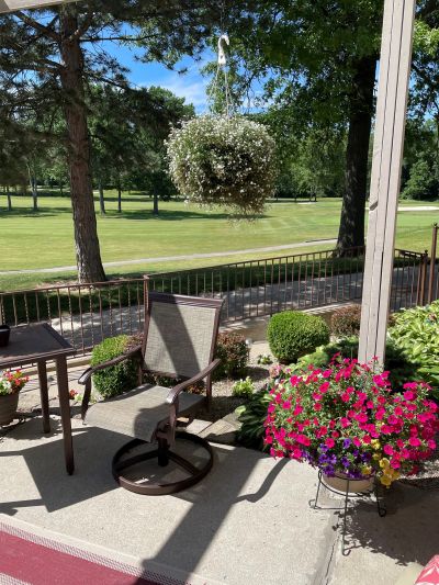 A cozy patio with chairs and colorful flowers overlooking a green lawn.