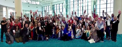 Large group of people posing together indoors, many waving at the camera.