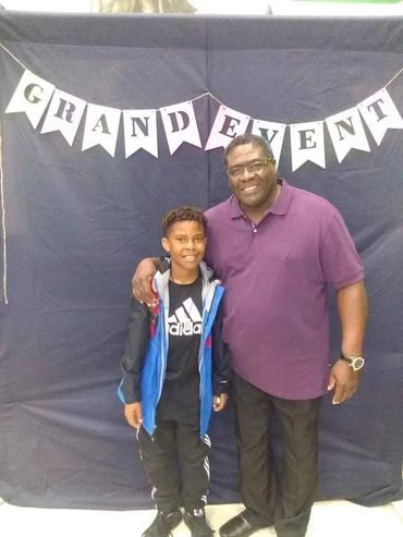 A man and boy smiling under a "Grand Event" banner.