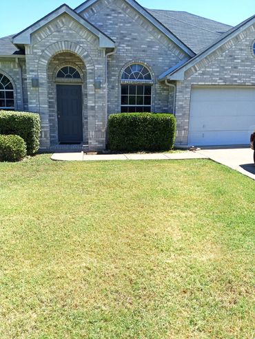 Front view of a brick house with green lawn and bushes.