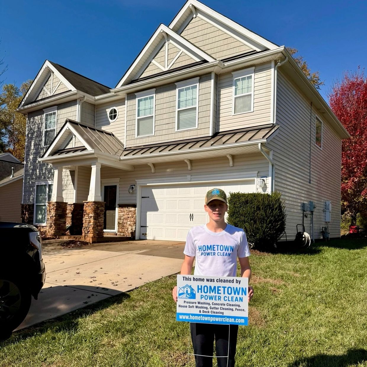 Young man stands in front of a clean house holding a promotional sign for power cleaning services.