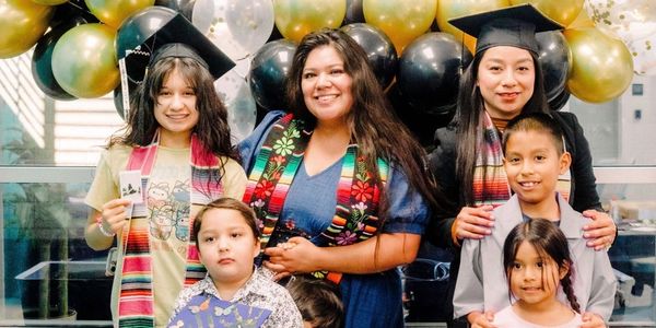 Two graduates with children, smiling amid balloons.