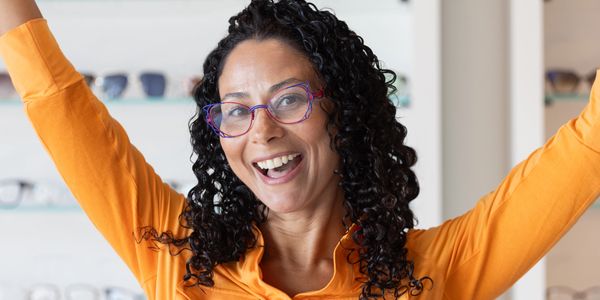 Smiling woman wearing colorful eyeglasses in an optical boutique, showcasing stylish eyewear options at SightCraft Eyecare in West Palm Beach