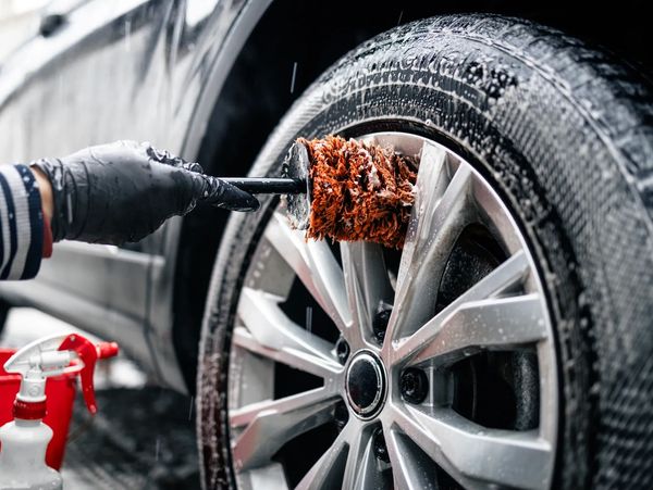 Person cleaning a car wheel with a brush and soap.