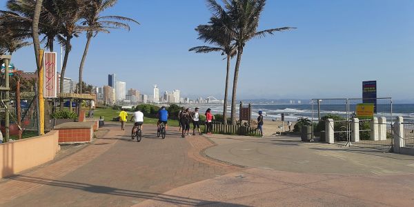 People biking and walking along a sunny beach promenade.