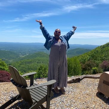 Joyful woman with arms raised, embracing a scenic mountain view under a clear blue sky.