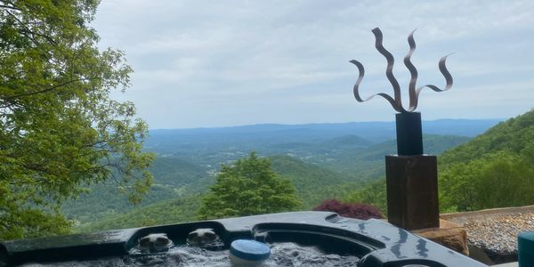 Hot tub with bubbling water overlooking a scenic mountain view and artistic sculpture.