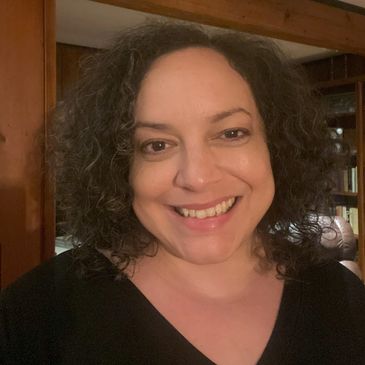 Smiling woman with curly hair in a cozy, wood-paneled room.