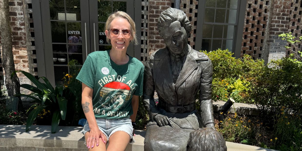 Woman sitting next to a bronze statue of a lady and a dog on a sunny day.
