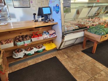 Small market counter with fresh vegetables and a meat display case.