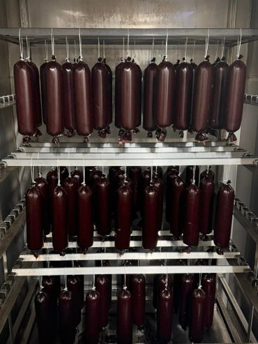 Rows of dark sausages hanging on metal racks in a smokehouse or curing room.