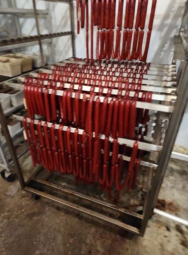 Rows of red sausages hanging on metal racks in a processing room.