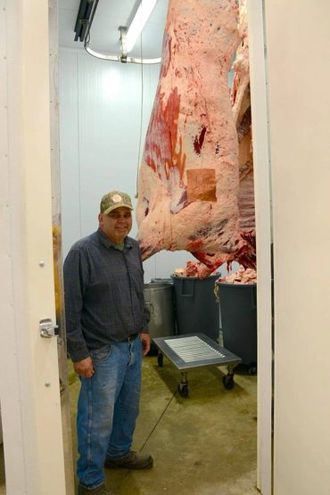A man stands in a meat processing room with large hanging meat carcasses.