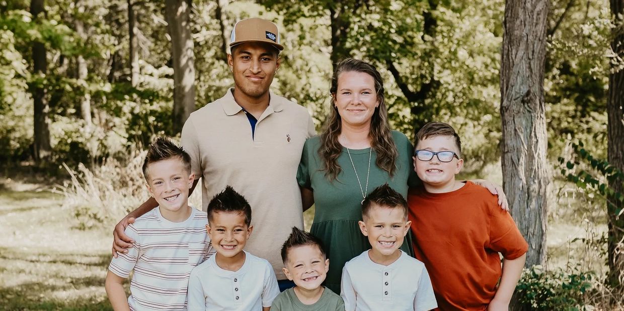 A happy family of seven posing outdoors in a wooded area.