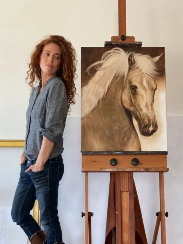Woman standing next to a horse painting on an easel.