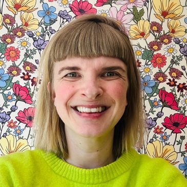 Smiling woman with blonde hair in front of a colorful floral background.