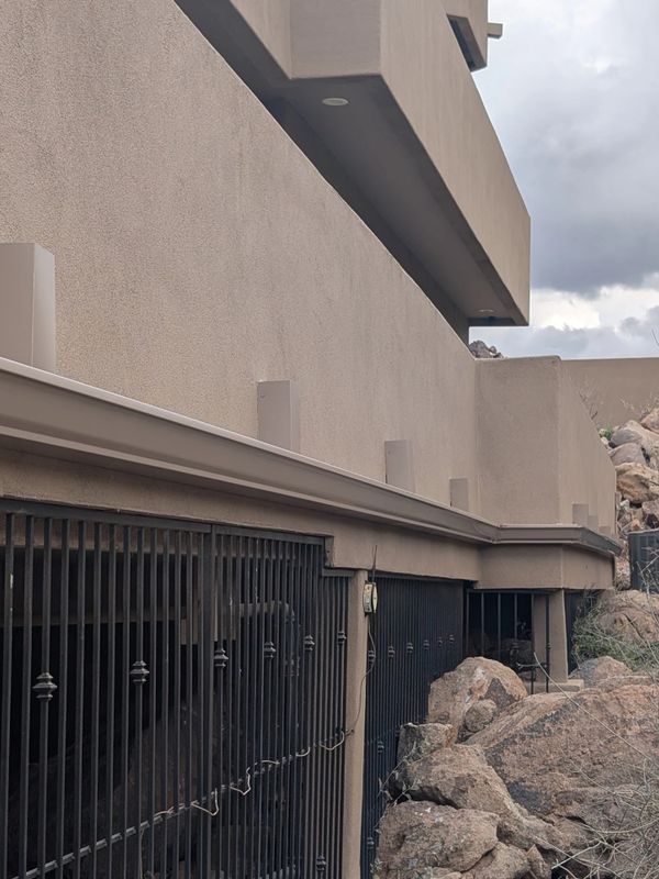 Modern building with metal barred windows and rocky surroundings under a cloudy sky.