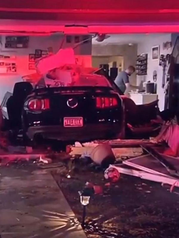 Car crashed through garage with debris scattered inside and person in background.