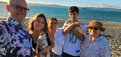 A happy family selfie on the beach with two small dogs and a scenic ocean backdrop.
