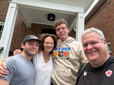 Four people smiling outdoors in front of a brick building.