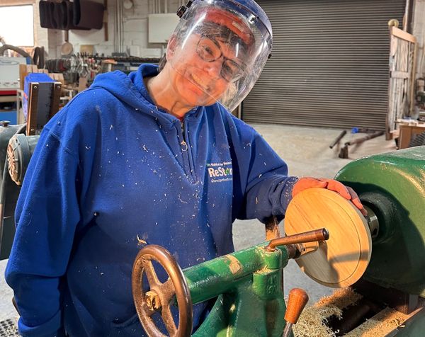 Person working on a wood lathe, shaping a round wooden piece.