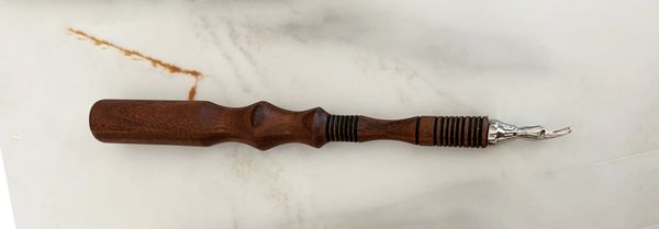 Handcrafted wooden tool with a metal tip on a marble surface.