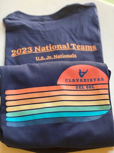 Two folded navy shirts with 2023 National Teams and Clavadistas Del Sol logos.