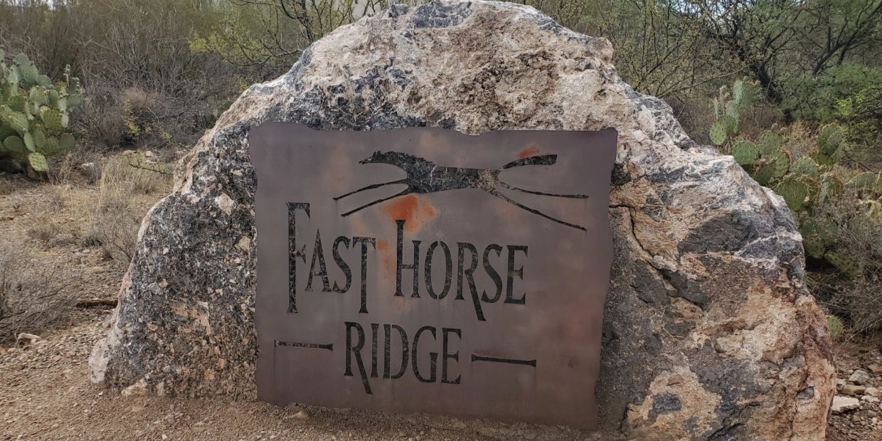 Rustic sign for Fast Horse Ridge on a large rock in a desert landscape.