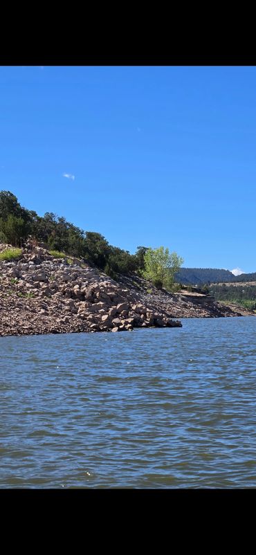 Rocky shoreline beside a calm lake under clear blue skies.
