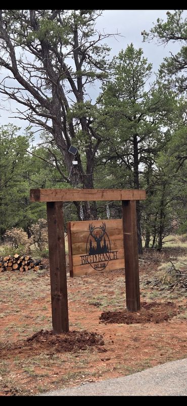 Wooden ranch sign hanging between two posts in a forested area.