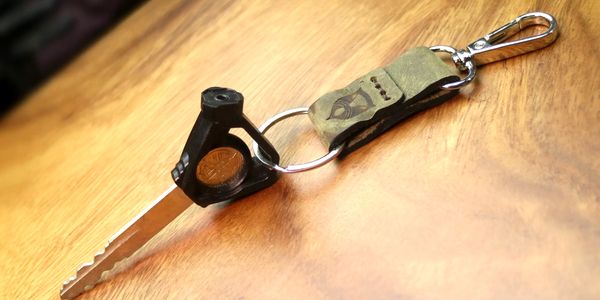 A key with a black plastic head and leather keychain on a wooden surface.