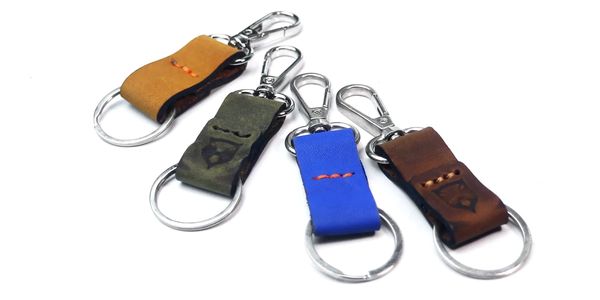 Four leather keychains in different colors with metal rings and clips.