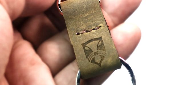 Hand holding a leather keychain with a metal ring and a fox logo.