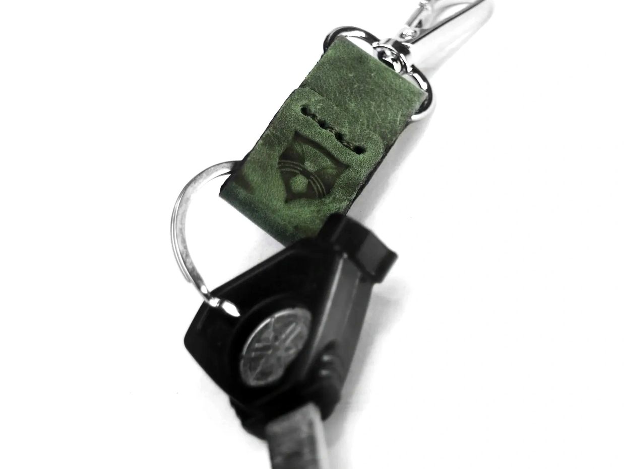 Close-up of a key with a green leather keychain on a white background.