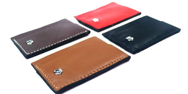Four leather card holders in brown, red, black, and tan colors with metal emblem.