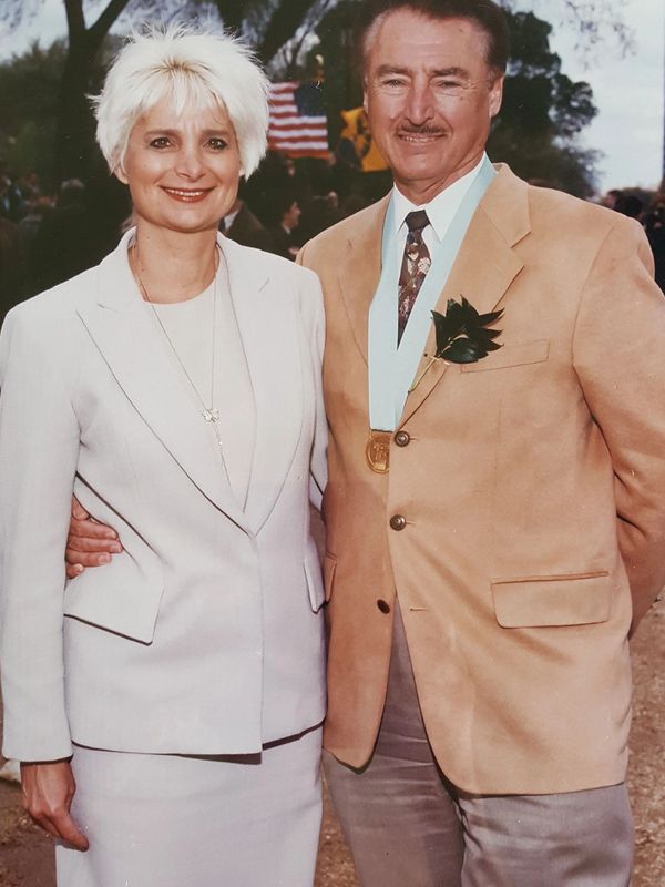 A smiling couple dressed formally, with the man wearing a medal.