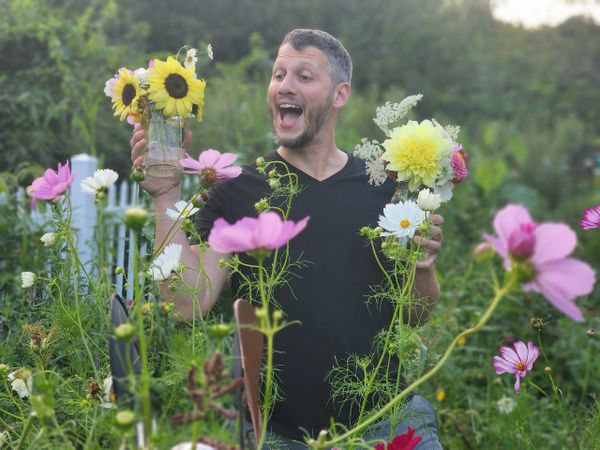 A joyful man holding two jars of colorful flowers in a garden.