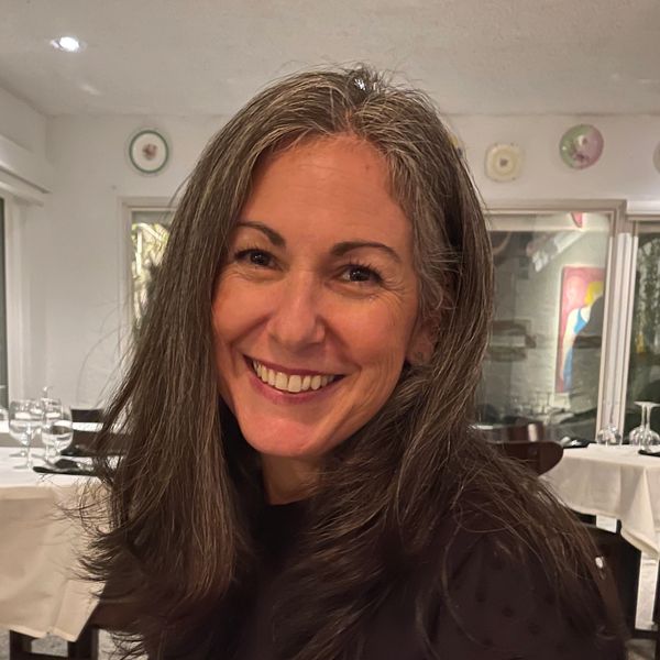 Smiling woman with long gray hair in a cozy restaurant setting.