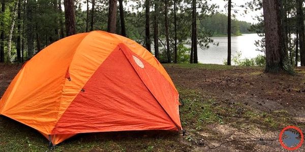 Orange tent pitched in a forest near a lake.