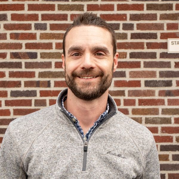 Smiling man standing against a brick wall background.